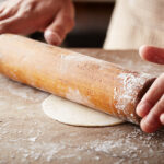 Hands baking dough with rolling pin on wooden table