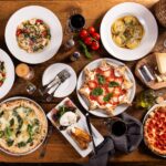 Big dinner table with italian food, pizzas and pastas
